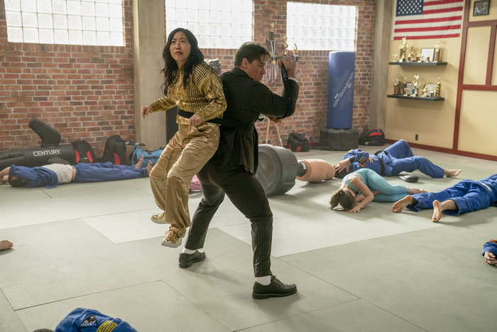 Awkwafina and John Cena in 'Jackpot!' She is tied to his back, her shoes about a foot above the ground as Cena holds a readying fight pose.